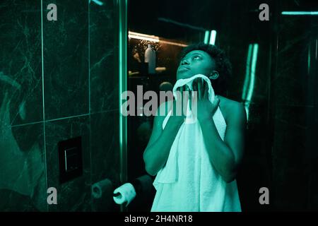 Belle femme africaine essuyant son corps avec une serviette après la douche tout en se tenant dans le bain Banque D'Images
