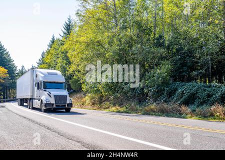 Semi-camion classique à capot blanc avec toit surélevé transportant des marchandises commerciales dans une remorque semi-remorque de camionnette sèche pour livraison sur la route sinueuse Banque D'Images