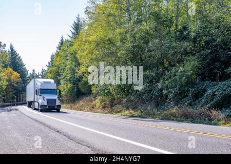 Semi-camion classique à capot blanc avec toit surélevé transportant des marchandises commerciales dans une remorque semi-remorque de camionnette sèche pour livraison sur la route sinueuse Banque D'Images