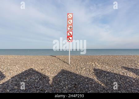 Ombres des huttes de plage projetant sur les galets de la plage de Cayeux-sur-Mer.Divers panneaux d'interdiction.Opal Coast, France Banque D'Images