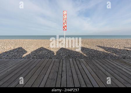 Ombres des huttes de plage projetant sur les galets de la plage de Cayeux-sur-Mer.Divers panneaux d'interdiction.Opal Coast, France Banque D'Images