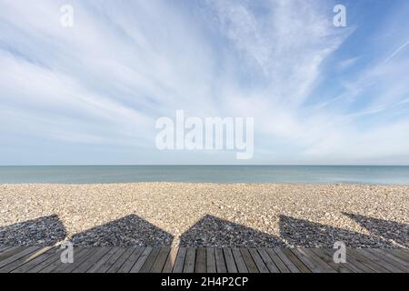 Ombres des huttes de plage projetant sur les galets de la plage de Cayeux-sur-Mer.Opal Coast, France Banque D'Images