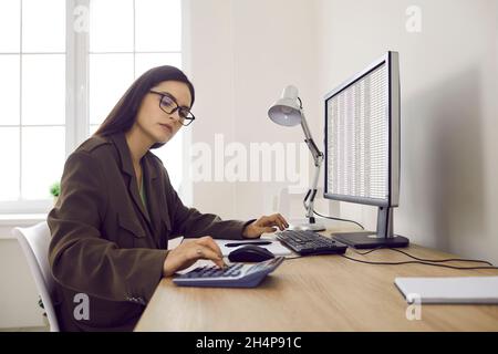 Expert-comptable professionnel sérieux en lunettes travaillant au bureau et utilisant un ordinateur et une calculatrice Banque D'Images