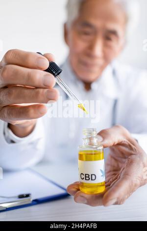 L'huile de CBD entre les mains d'un médecin asiatique flou près du presse-papiers en clinique Banque D'Images