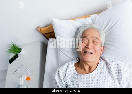 Vue de dessus d'un patient asiatique gai allongé sur le lit dans le service hospitalier Banque D'Images