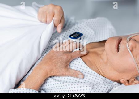 Vue rognée d'un homme âgé malade avec canule nasale et oxymètre de pouls allongé sur le lit en clinique Banque D'Images