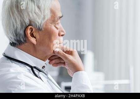 Vue latérale d'un médecin asiatique senior qui regarde loin dans la clinique Banque D'Images