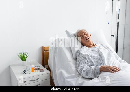 Malade asiatique allongé sur le lit près des pilules et de l'eau dans la salle d'hôpital Banque D'Images