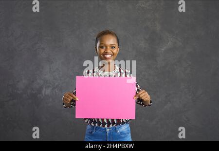 Portrait d'une jeune femme noire souriante et heureuse tenant une bannière de maquette rose vierge Banque D'Images