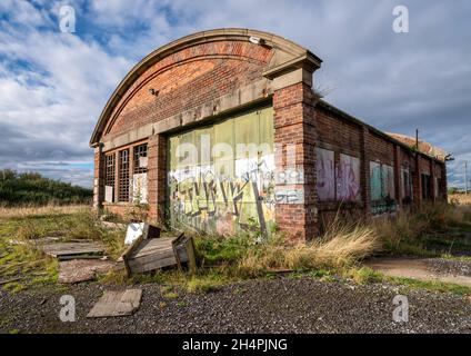 Un vieux garage en briques a maintenant abandonné dans un sol de déchets avec des graffitis sur un ciel bleu ensoleillé de nuage. Banque D'Images