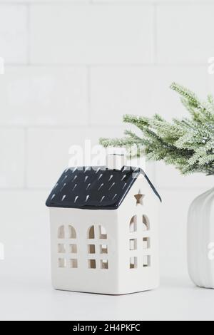 Décoration intérieure de Noël nordique.Petite maison en céramique et vase avec branche de sapin sur table blanche.Maison confortable, style scandinave.Hiver Banque D'Images