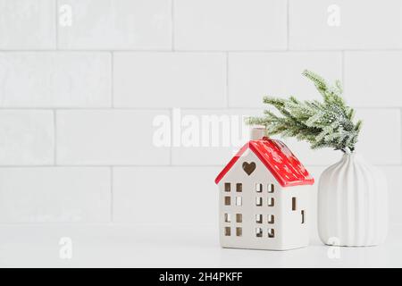 Décoration de Noël nordique sur fond de mur en brique.Petite maison en céramique et vase avec branche de sapin.Maison confortable, concept vacances d'hiver hygge. Banque D'Images