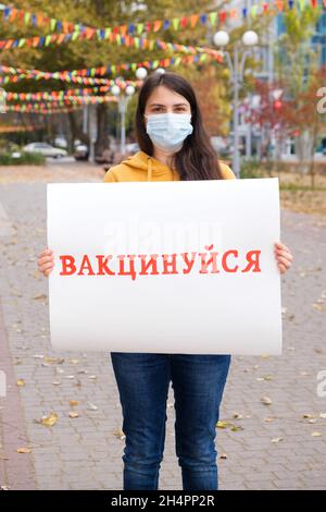 Une femme dans un masque médical tient une affiche avec une inscription, traduite de l'ukrainien se faire vacciner Banque D'Images
