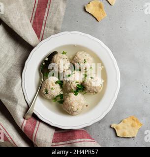 Soupe de boulettes de matzo de poulet maison avec persil et ail dans une simple plaque de céramique blanche sur fond de pierre grise ou de béton.Passe juif traditionnel Banque D'Images