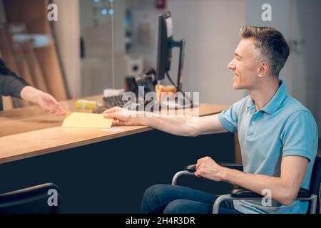 Homme en fauteuil roulant tenant l'enveloppe près du comptoir Banque D'Images