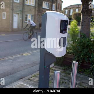 Un cycliste passe devant les points de recharge des véhicules électriques dans un parking public du village de Northowram, dans le West Yorkshire, près de Halifax, à Calvaire.Situé contre la goutte arrière de maisons traditionnelles en pierre. Banque D'Images