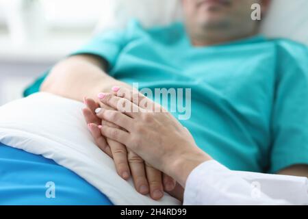 Les mains des médecins tiennent les mains du patient allongé dans la salle Banque D'Images