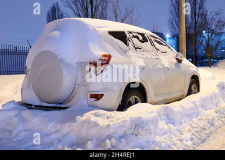 Voiture blanche recouverte de neige la nuit.Véhicule utilitaire sport stationné dans la cour.Ville après la tempête de neige.Vue arrière. Banque D'Images