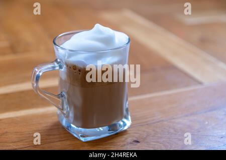 une tasse de café en verre recouverte de mousse de lait blanche sur une surface en bois Banque D'Images