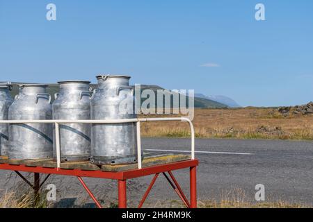 Vue rapprochée de quelques churns de lait sur un stand de churn de lait le long de l'une des routes de la zone agricole de l'Islande avec des montagnes et paysage volcanique i Banque D'Images