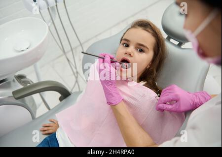 Vue en hauteur d'une petite fille mignonne à l'arrivée dentaire dans la clinique dentaire blanche avec équipement moderne.Dentiste pédiatrique examinant les dents de l'enfant à l'aide de steri Banque D'Images