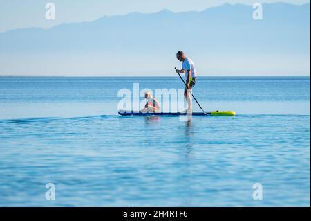 Le père et la fille à bord du SUP se tiennent debout pagayer pendant les vacances.Une famille active à cheval sur des planches SUP et à pagayer dans l'océan dans la belle soirée.Athlet Banque D'Images