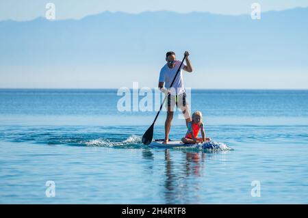 Le père et la fille à bord du SUP se tiennent debout pagayer pendant les vacances.Une famille active à cheval sur des planches SUP et à pagayer dans l'océan dans la belle soirée.Athlet Banque D'Images