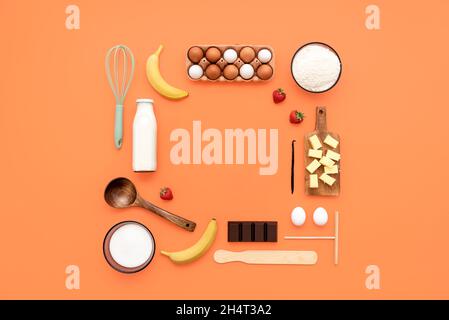 Les aliments sont composés d'ingrédients de crêpes et d'ustensiles de cuisine sur fond orange.Faire des crêpes à plat, les outils de cuisine, et les ingrédients disposés avec Banque D'Images