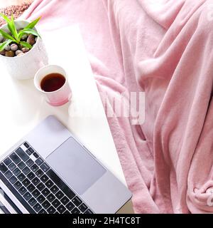 ordinateur portable et une tasse de thé sur une table blanche avec une couverture à cueillir à proximité. concept d'hygge. Banque D'Images