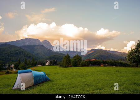 Tente de camping placée sur le champ de prairie d'herbe verte contre le paysage des montagnes tatra au coucher du soleil et des nuages spectaculaires, aventure dans la nature sauvage Banque D'Images