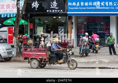 Un Chinois sur son véhicule utilitaire à trois roues dans la rue de Yangshuo, en Chine. Banque D'Images