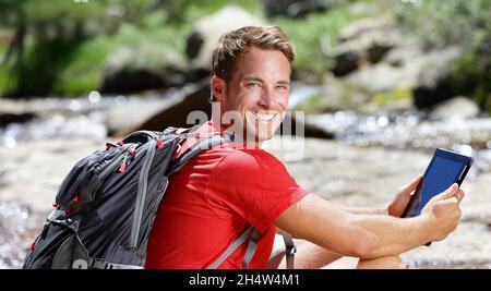 Tablette ordinateur homme randonnée dans la forêt des États-Unis en plein air à l'aide d'une application de voyage ou d'une carte sur un appareil portable pendant la randonnée.Randonneur mâle caucasien se relaxant sur un Banque D'Images