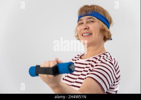 Bonne vieille femme faisant des exercices de forme physique avec des haltères sur un fond blanc. Femme âgée en forme physique pour maintenir la santé. Banque D'Images