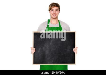 Le propriétaire d'une petite entreprise montrant un tableau noir vierge affiche vide portant un tablier vert.Un jeune propriétaire de boutique charmant, isolé sur fond blanc souriant Banque D'Images