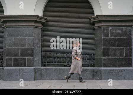 Une femme descend une rue à l'architecture ancienne au centre de l'image, portant une longue veste.Copier l'espace Banque D'Images