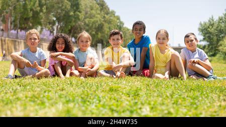 Groupe d'amis enfants heureux se reposant sur l'herbe ensemble dans le parc Banque D'Images