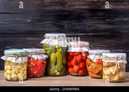 Tomates cerises marinées maison, concombres, champignons, ail, aubergines,Poivrons rouges en pots sur étagère en bois aliments en conserve et fermentés faits maison co Banque D'Images