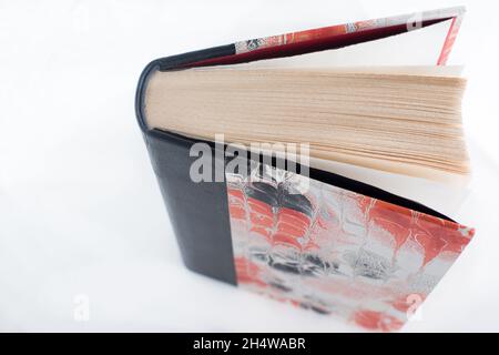 Beau livre à main avec papier en cuir et aquarelle en rouge et noir.Arrière-plan blanc. Gros plan par le dessus. Banque D'Images