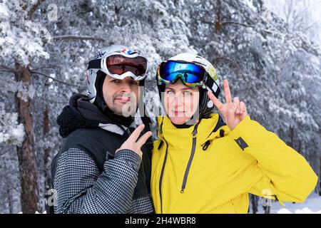 Homme et femme caucasiens d'âge moyen heureux en casque de ski et lunettes de protection sur le fond d'une forêt enneigée.Repos hivernal actif.Des vêtements brillants pour un A. Banque D'Images