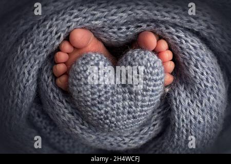 Jambes, orteils, pieds et talons d'un nouveau-né.Enveloppé dans une couverture tricotée grise.Coeur tricoté dans les jambes de bébé. Banque D'Images