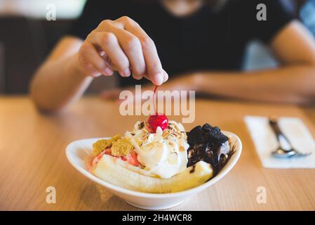 Femelle à la main mettant de la cerise rouge sur des sundae à la banane maison. Banque D'Images