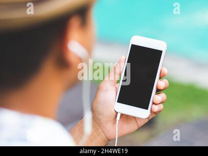 Un jeune homme écoute de la musique sur son smartphone tout en étant assis près de la piscine. Concept de détente. Banque D'Images