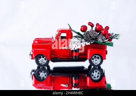 Bouquet de Noël avec baies dans un camion de Noël rouge sur fond blanc, reflété dans une surface miroir.Concept - carte de vœux pour Noël an Banque D'Images