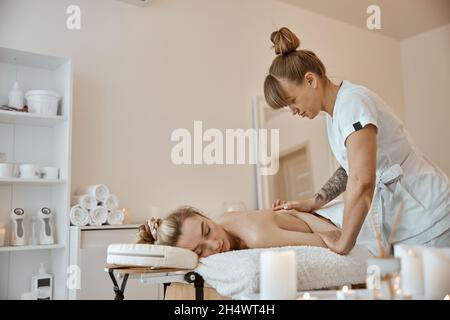 Professionnel confiant maître de massage fait des procédures à la femme caucasienne dans le cabinet moderne minimaliste Banque D'Images