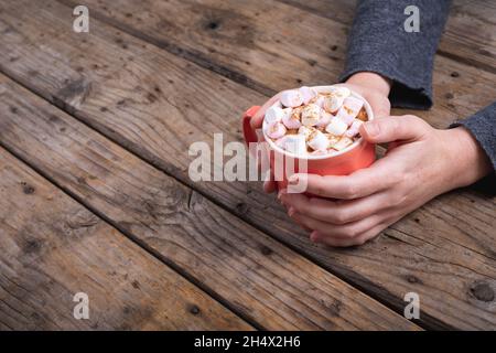 Les mains de la femme sont coupées et tiennent une tasse de boisson chaude au chocolat et des guimauves à la table avec un espace de copie Banque D'Images