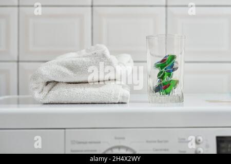 Serviette avec capsules de lessive et détergent sur le dessus du lave-linge.Capsules de lessive ou également connu sous le nom de gel de lessive en capsules et serviette blanche Banque D'Images