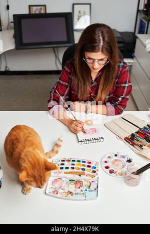 Une femme illustratrice travaillant au bureau à domicile avec son chat sur le bureau Banque D'Images