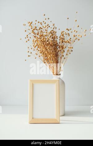 Maquette de cadre photo et vase avec lin séché sur table blanche.Décor scandinave et scandinave fixe. Banque D'Images