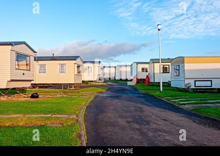 Des caravanes rectangulaires de couleur crème espacées de manière égale avec des pierres de pavage entre l'herbe tonée pour le stationnement de voiture de chaque côté d'une route étroite tarmac Banque D'Images