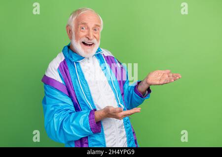 Photo de l'homme assez impressionné senior porter costume sportif souriant tenant les bras vide espace isolé couleur vert arrière-plan. Banque D'Images